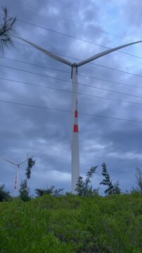 Vertical video of wind turbines spinning at twilight against dramatic stormy sky with green bushes in Quy Nhon Vietnam