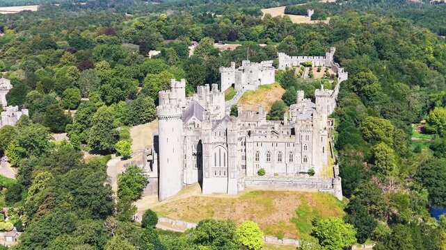 Arundel castle drone push-in as camera stays locked to the fortress, tilting down while approaching above treetops and landscaped grounds in West Sussex, England.
