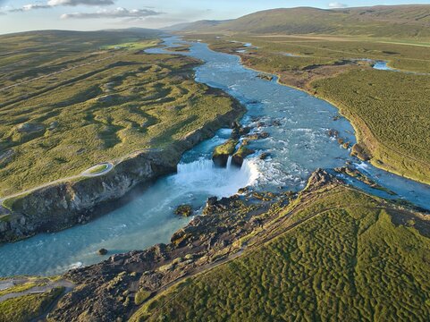 Aerial view of Godafoss Waterfall with its horseshoe-shaped cascade, turquoise river water, and surrounding mossy volcanic landscape in Godafoss, Thingeyjarsveit, Iceland.