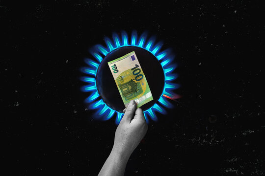  gas oven - orange tongues of blue flame of a gas burner burn the money.  Hand holding 100 Euro bill as a sign of rising energy costs.