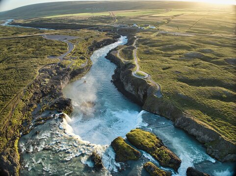 Aerial view of Godafoss Waterfall with its cascading water flowing through the rugged volcanic landscape under soft golden hour light in Godafoss, Thingeyjarsveit, Iceland.