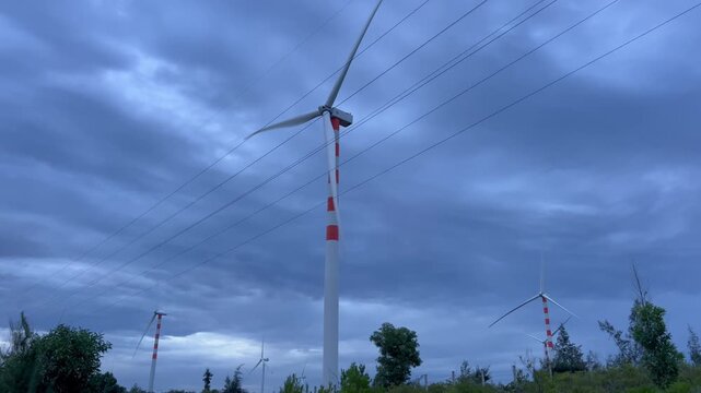Handheld wide shot of multiple wind turbines spinning at twilight under dramatic stormy sky in Quy Nhon Vietnam