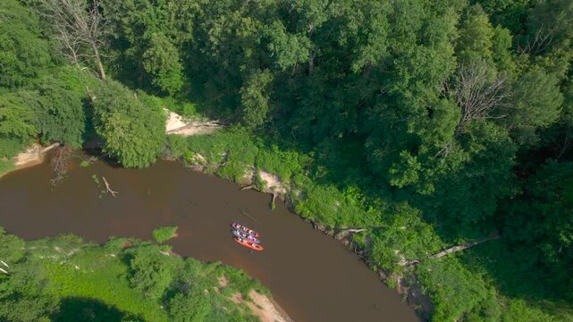 Friends kayaking follows four inflatable kayaks clustered together around a shaded brown river bend bordered by dense summer forest as the drone glides laterally above the paddlers outdoors