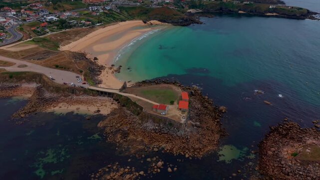 Aerial - Rocky headland with chapel buildings beside a curved sandy beach in Pontevedra Spain