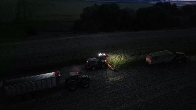 Aerial View of Nighttime Corn Silage Harvest with Forage Harvester and Tractors