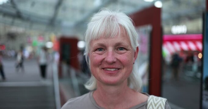 Caucasian senior woman smiling on camera at bus station - Urban, travel and city lifestyle concept - Main focus on face - UGC content