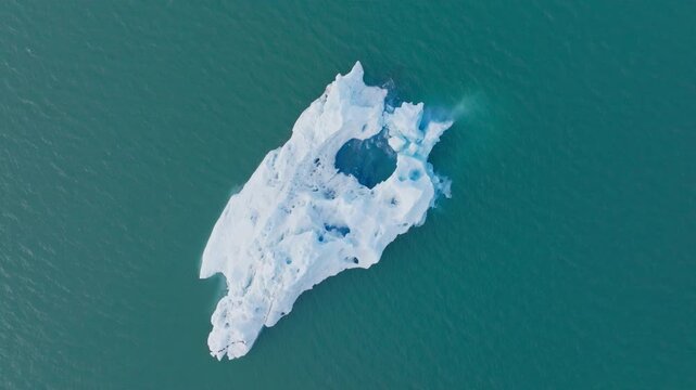 Top down aerial of iceberg floating on turquoise lake water in Iceland