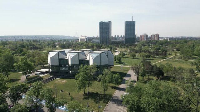 Low drone shot across Usce Park with lush greenery and brutalist buildings of New Belgrade, Serbia.