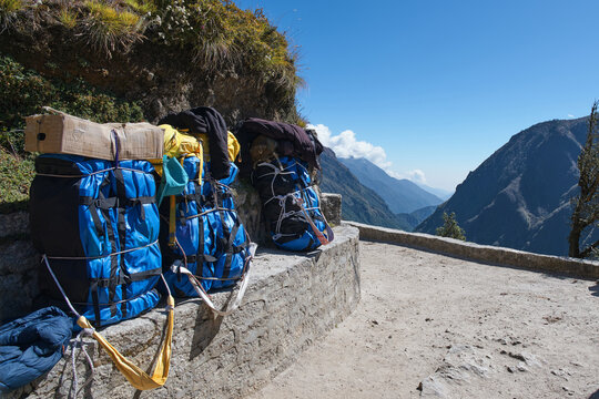 Heavy duffel bags and backpacks of Sherpa porters resting on a stone wall along the scenic trail to Everest Base Camp in Nepal