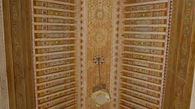 Camera tilts down ornate wooden ceiling with geometric patterns in Marrakesh interior