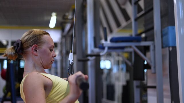 Experience the focus and determination of a middle-aged woman as she performs controlled pulldown exercises on a lat machine, targeting her lats for a strong upper body workout.