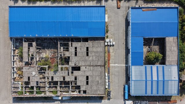Aerial view of industrial buildings in the Severna Zona, featuring one structure with a damaged roof and internal vegetation alongside a building with a blue metal roof in Pancevo, Serbia.