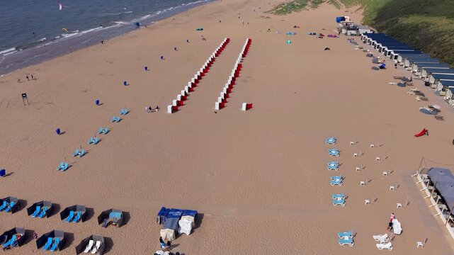 Aerial view video clip of Katwijk aan Zee sandy beach, beach resort loungers, red beach cabins, beach houses, coastal sand dunes, and North Sea waves in South Holland, Netherlands