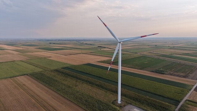 Aerial view of a wind turbine standing in the middle of vast agricultural fields under a soft sunset sky in Crepaja, Vojvodina, Serbia.