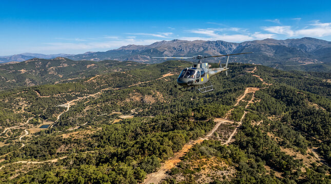 Helic&oacute;ptero sobrevolando un bosque mediterr&aacute;neo para vigilar y prevenir incendios forestales, mostrando gesti&oacute;n y protecci&oacute;n del territorio.