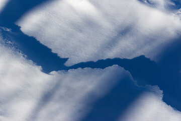 Close-up view of pristine white snow crust with soft blue shadows, creating abstract geometric patterns on a frozen winter landscape surface under bright daylight conditions © PhotoChur
