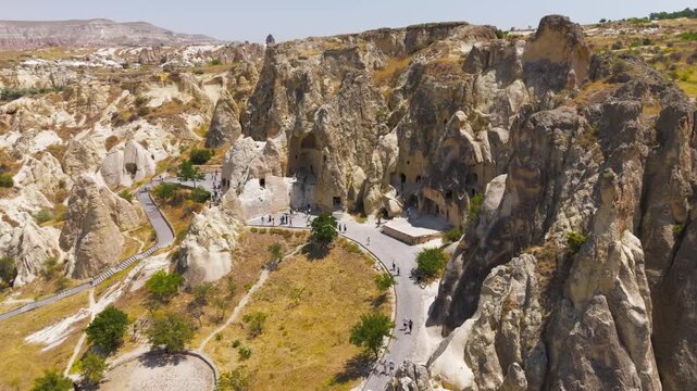 Goreme, Nevsehir, Turkey. Goreme Open Air Museum, ancient rock-cut churches and monastic caves in volcanic tuff, aerial view with tourists exploring under bright summer sun. Aerial View, Point of int