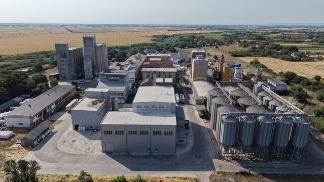 Aerial view of the industrial grain processing facility in the severna zona with large metal silos, warehouses, and surrounding agricultural fields in Pancevo, Serbia.