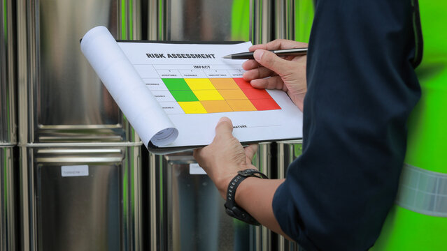 Focused industrial inspector diligently conducts safety audit using clipboard with risk assessment matrix chart near chemical storage