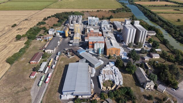 Aerial view of the Severna zona industrial facility featuring large grain silos, warehouses, and trucks parked on site near a canal in Pancevo, Serbia.