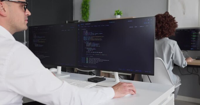 Programmer coding software on computer monitors in office. A focused developer and coder collaborate with colleagues. Modern workspace and screens boost teamwork. Concept of teamwork and coding.