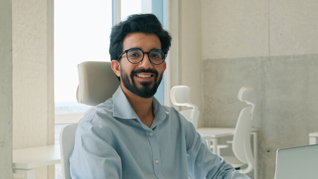 Successful Arabian Indian business man working on laptop looking at camera indoor office entrepreneur typing project startup smiling muslim businessman software engineer employer digital online work