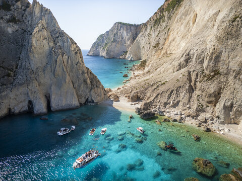 Aerial view of tourist boats floating in the turquoise waters of a secluded cove surrounded by towering limestone cliffs in Zakinthos, Greece.