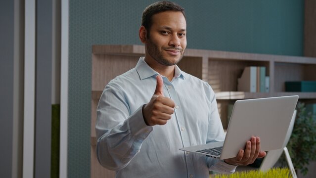 Indian Arabian business man working on laptop modern corporate office showing thumb up positive gesture male worker approve online work businessman employee recommendation agree support computer desk