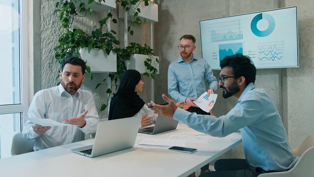 Diverse four multiethnic business team men businesswoman in hijab discussing ideas indoor office briefing analyzing strategy interactive board talking brainstorm workflow colleagues meeting teamwork