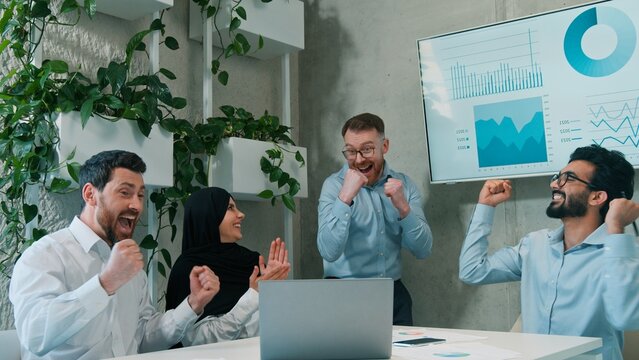 Happy multiethnic business team celebrating victory success laptop office coworkers win deal finance Arabian Indian Caucasian men muslim woman in hijab teamwork achievement corporate workplace indoor