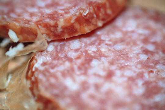Macro close-up shot of thin sliced cured salami sausage on wooden cutting board