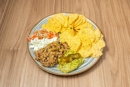 Nachos with ground meat guacamole sour cream salsa and jalape&ntilde;os on striped plate
