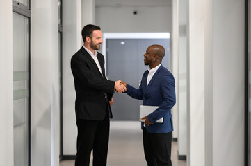 Fototapeta premium Two businessmen shaking hands after successful business meeting in modern office corridor