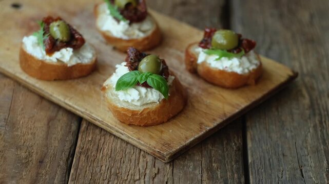 Bruschetta or crostini with cream cheese, sun-dried tomatoes, olives, fresh herbs. Tasty healthy snacks.
