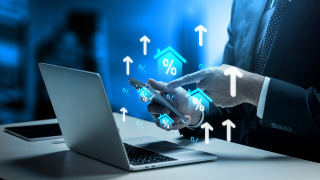 Businessman analyzing rising mortgage interest rates on a smartphone and laptop, featuring digital house percent icons and upward arrows. Concept of house and property tax