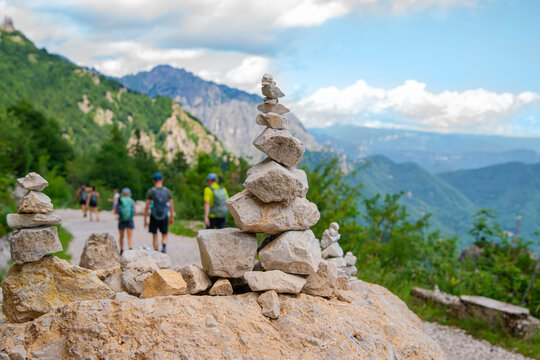 Close up of a stone pyramid or rock cairn on a hiking trail path with blurred hikers walking in mountains on a sunny summer day
