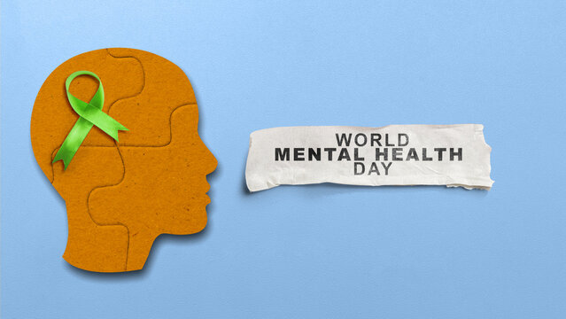 Orange puzzle head with green awareness ribbon and torn paper reading World Mental Health Day on blue background. Concept of World Mental Health Day