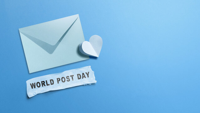Minimalist World Post Day concept featuring a blue envelope, a paper heart, and torn paper text on a blue background with copy space. Concept of World Post Day