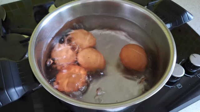 Brown chicken eggs are boiled in a stainless steel pot on a gas stove