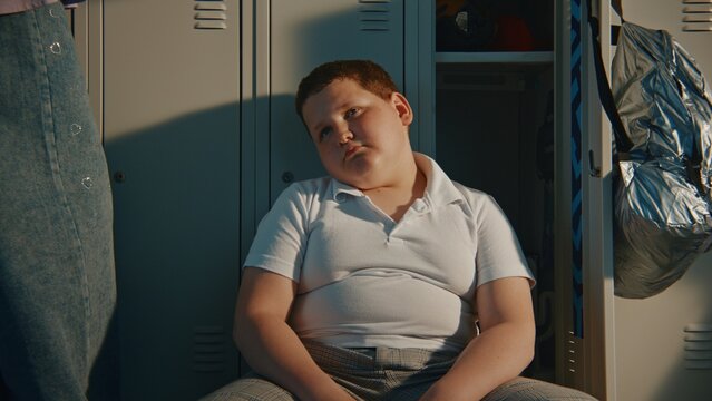 Young Schoolboy Spending Time Alone beside Personal Locker while Classmates Nearby Outside Frame. Concept of Friendship, Social Inclusion, Childhood Emotions, Education, and Student Wellbeing.