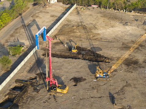 Aerial view of the Waste to Energy Facility Construction Project with a crawler crane, piling rig, and excavator on a dirt site in Kecamatan Denpasar Selatan, Bali, Indonesia.