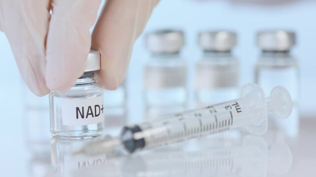 Gloved hand holding nad therapy vial near medical syringe for healthcare wellness medicine treatment inside laboratory clinic