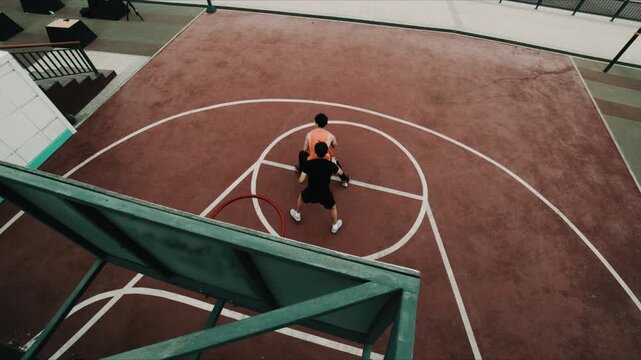 Two young men play basketball on an outdoor court with one dribbling during a competitive game