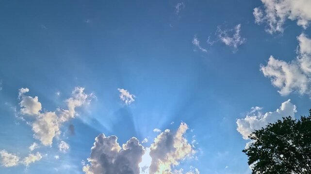 View of the sky with the sun behind the clouds creating sunrays and a plane flying across