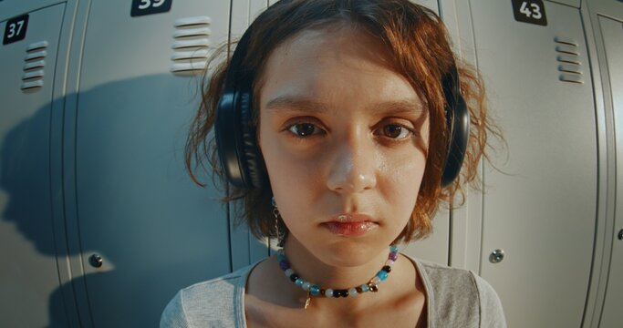 Portrait of Teenage Girl Wearing Headphones Looking Directly While Standing Near School Lockers Bathed in Warm Golden Hour Light. Confident Expression, Youth Culture, Modern Gen Z Student Lifestyle.