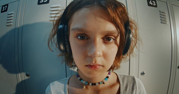 Portrait of Teenage Girl Wearing Headphones Looking Directly While Standing Near School Lockers Bathed in Warm Golden Hour Light. Confident Expression, Youth Culture, Modern Gen Z Student Lifestyle.