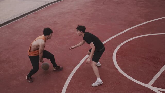 Young men play competitive streetball on outdoor court with dribbling action