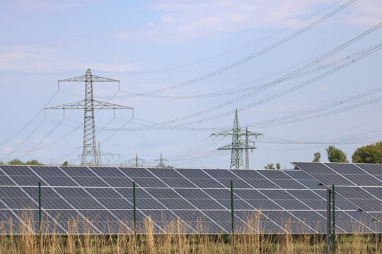 Solar panels in the foreground with high voltage transmission power pylon and rural landscape in the background