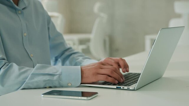 Happy Arabian Indian business man working online laptop office table coding software moving shot male employer programmer businessman guy typing project remote work computer mobile phone desk indoor
