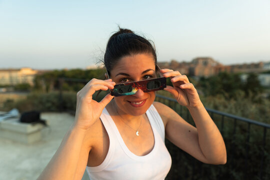 Woman holding solar eclipse glasses, smiling outdoors
